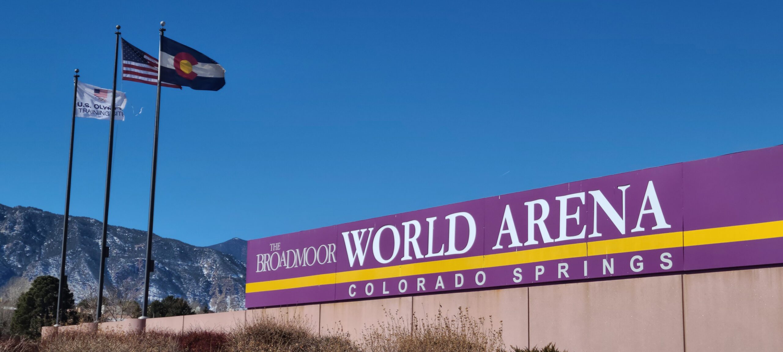 The Broadmoor World Arena sign in Colorado Springs with U.S., Colorado and U.S. Olympic Training Site flags and the mountains behind